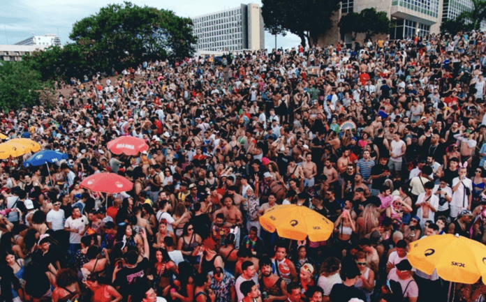 Grande aglomeração de foliões no Carnaval de Brasília 2026 com blocos e cores vibrantes.