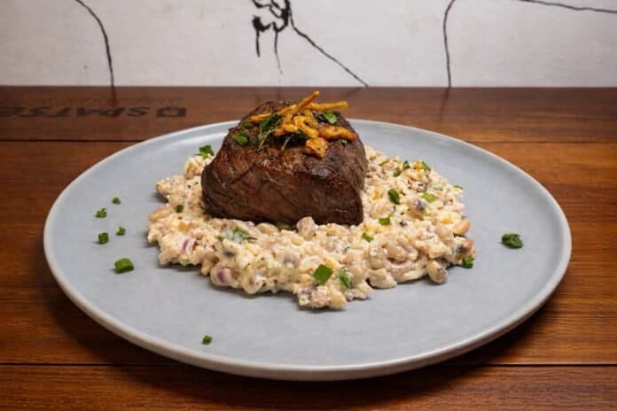 Carne suculenta sobre risoto de queijo com cebolas e ervas frescas.