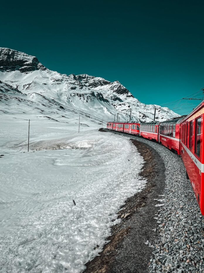 red train moving near snow covered mountain