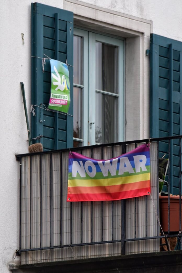 a rainbow flag with a sign no war attached to a balcony