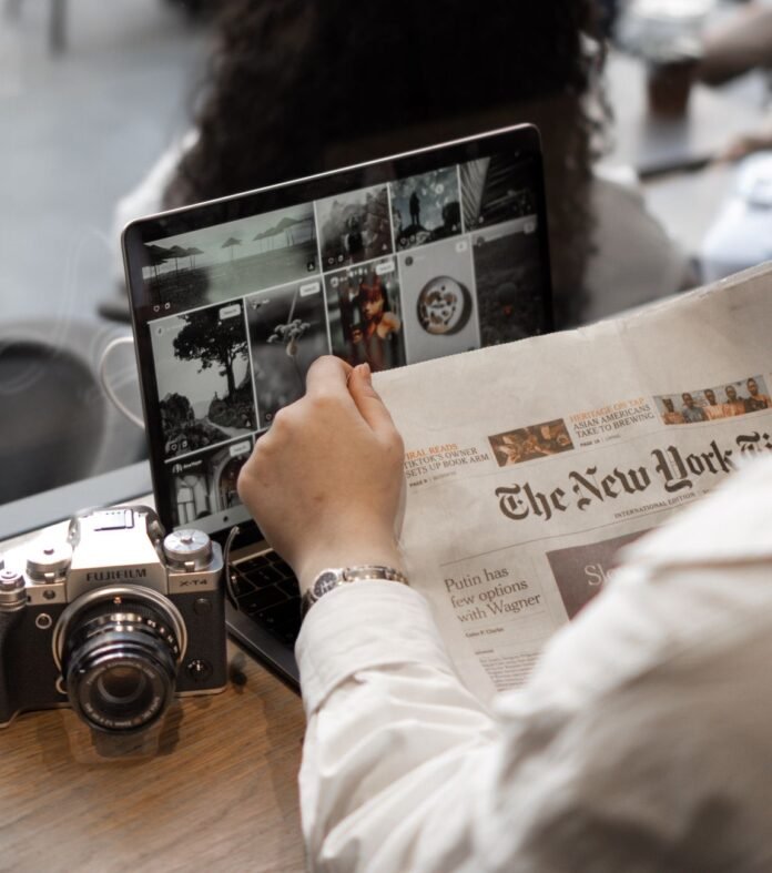 person reading a newspaper and using a laptop and a camera